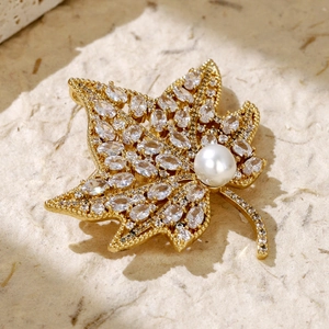 Close-up of golden leaf brooch with sparkling zircons and a white pearl on paper