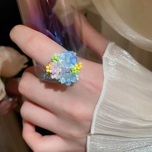 Dettaglio di un anello a fiore in resina con petali blu e perline cangianti