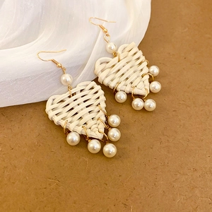 Détail de boucles d'oreilles cœur en raphia tressé avec perles de style bohème chic