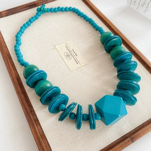 Detail of turquoise faceted geometric pendant and wooden beads on a linen display tray