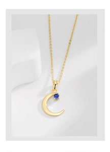 Detailed shot of a gold crescent moon necklace with a square deep blue stone on a white block