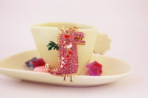 Détail d'un porte-clés dragon rose orné de strass avec des ailes vertes et métal doré