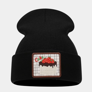 Close-up of black knitted beanie featuring a strawberry cake embroidery patch detail
