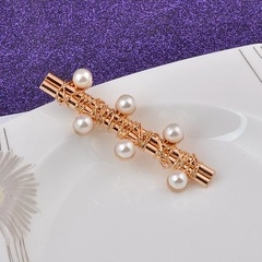 Detailed view of long gold metal hair clip with delicate wire wrap and white pearls