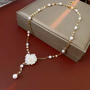 Detail of elegant gold Y-shaped necklace with white pearls and flower pendant on gift box