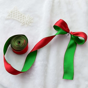 Red and green Christmas satin ribbon roll with a handmade bow on white fur background