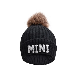 Detail of black knit hat featuring brown faux fur pompom and white MINI letter embroidery