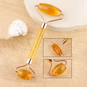 Detail of yellow resin dual-head facial roller with rose gold metal frame on a marble base