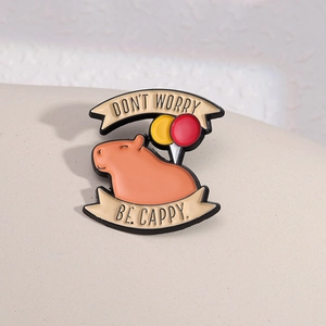Cute enamel capybara pin with balloons and Don't Worry Be Cappy text on a beige base