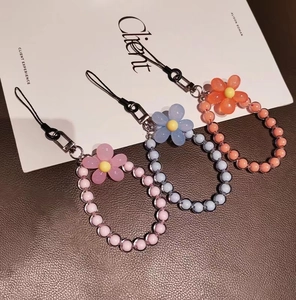 Detail view of colorful beaded macaron flower phone straps on a textured leather surface