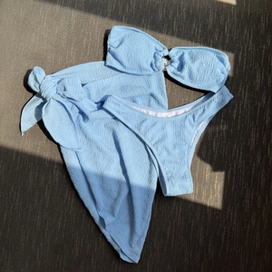 Three-piece sky blue textured bikini set with bandeau top, metal ring, and wrap skirt