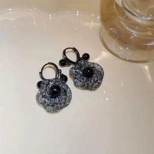 Macro detail of black rose mesh earrings with zircon accents and dark metallic texture