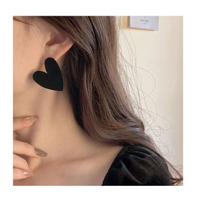 Close-up of model wearing black heart-shaped flocked stud earrings with velvet texture