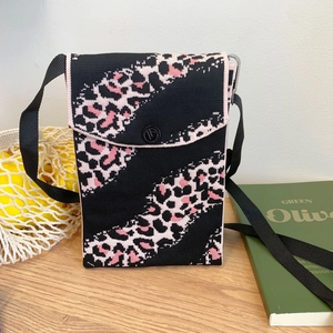 Detail shot of black knitted phone bag with pink leopard print on a wooden desk