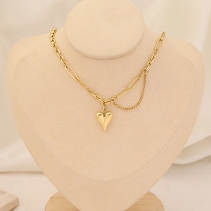 Layered gold heart pendant necklace with paperclip chain on a beige mannequin