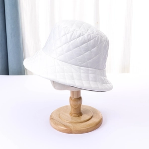 Detailed view of white quilted bucket hat featuring a classic diamond pattern on a wooden stand