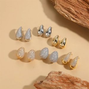 Elegant gold and silver waterdrop earrings with zircon crystals on a warm textured background