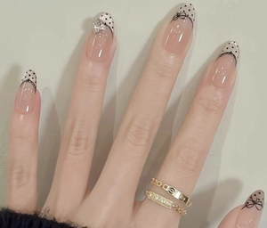 Detail of pink French almond press-on nails with black polka dots, bows and rhinestone