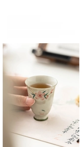 Close-up of hand holding a ceramic teacup with hand-painted peach blossoms and high-foot base