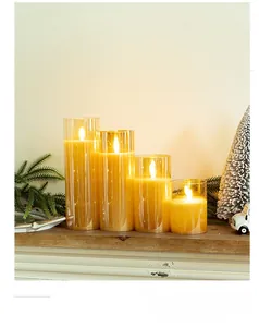 Four LED flameless candles in glass cylinders on wooden table with pine branches