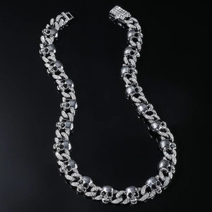 Men's punk style silver Cuban chain necklace with iced out skull charms on black background