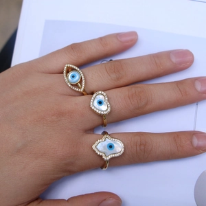 Detail of three gold Hamsa and Evil Eye rings with zircons and mother of pearl on a hand