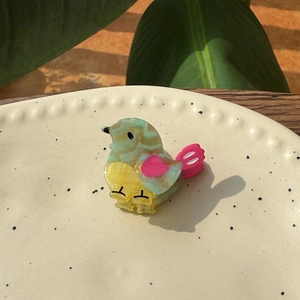 Chic mini bird hair clip made of marbled acetate with colorful wings on a ceramic tray