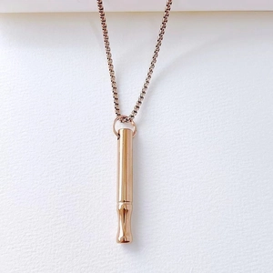 Detail showing a rose gold mindfulness breathing whistle pendant on a box chain.