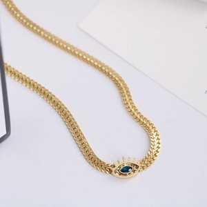 Gold evil eye necklace with deep blue stone and woven chain on minimalist white backdrop