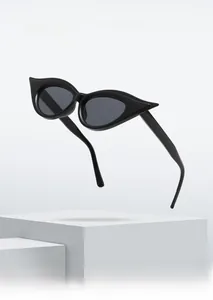 Detail of black cat-eye sunglasses with wing-shaped frames on a minimalist white pedestal
