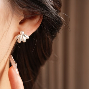 Close-up of a silver flower stud earring with a pearl on model ear in soft lighting