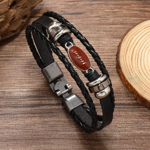 Close-up of vintage multilayer braided leather bracelet with rugby ball charm on wood