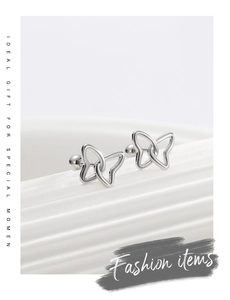 Macro detail of silver butterfly and heart stud earrings on a textured backdrop