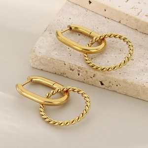 Detail of gold-plated twisted hoop earrings on textured stone and beige fabric