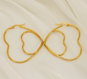 Detail of double-layered hollow heart gold hoop earrings on elegant white satin fabric