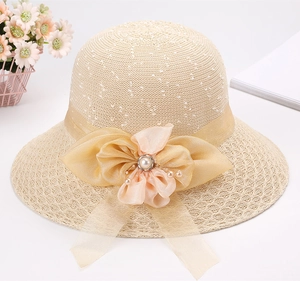 Dettaglio cappello di paglia beige con fiocco in organza dorata e perla centrale