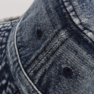 Dettaglio macro delle cuciture in denim e degli occhielli ricamati sul cappello pescatore