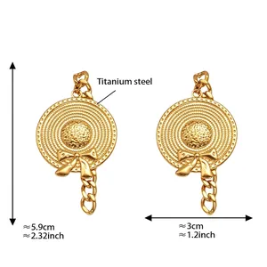 Detail view of gold straw hat earrings with bow and chain accents in titanium steel
