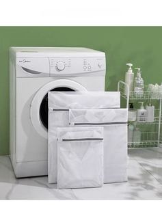 Detailed view of three mesh laundry bags with grey zippers set against a washing machine