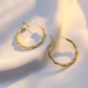 Macro shot of gold hoop earrings with sparkling cubic zirconia on soft silk background