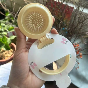 Portable cream-colored folding hairbrush with mirror featuring pink bow design