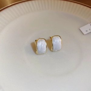 Detailed macro view of minimalist golden stud earrings with elegant white glaze inlay