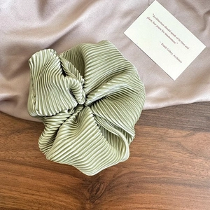 Detail of sage green pleated satin scrunchie with soft sheen and wavy texture