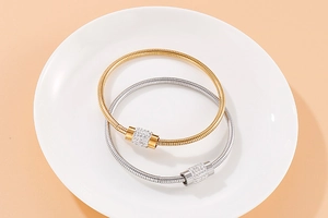 Détails de bracelets cylindriques dorés et argentés sertis de strass sur plateau blanc