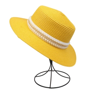 Detail of yellow woven straw hat with pearl and gold chain band on display stand