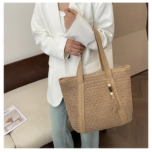 Detail shot of straw tote bag featuring woven texture and decorative tassel with wooden beads