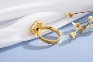 Detailed side view of a gold flower ring with a white shell inlay on silk fabric