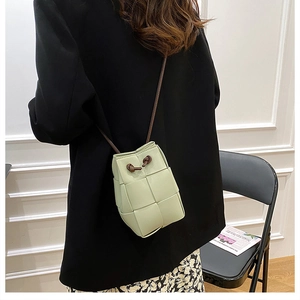 Detail of light green woven bucket bag showing shoulder strap and crossbody fit on model