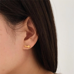 Close-up of a delicate gold bow stud earring on a model's ear with high-quality metal finish
