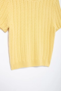 Dettaglio di un maglione giallo a maniche corte in maglia con trama a trecce fitte